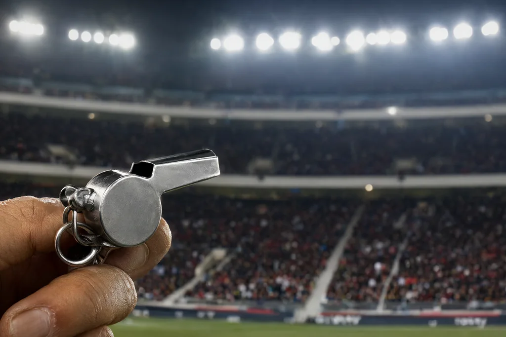 Referee whistle held up against a floodlit stadium background